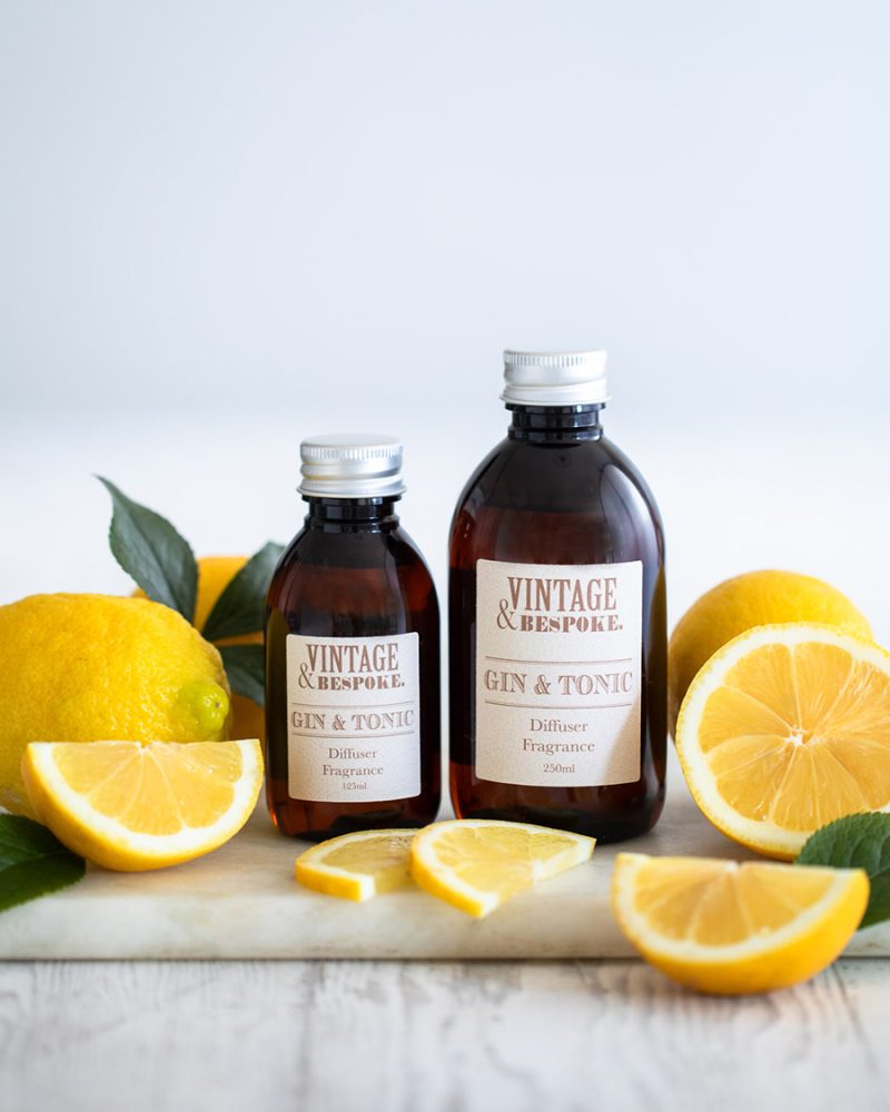 Gin and Tonic diffuser fragrance bottles with fresh lemons and citrus slices styled on a light surface